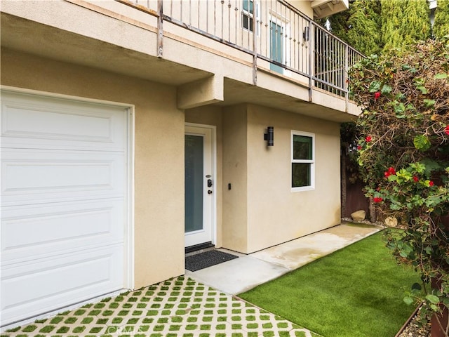 doorway to property with a garage, a lawn, and a balcony