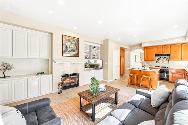 living room with arched walkways, light tile patterned flooring, built in shelves, a fireplace, and recessed lighting