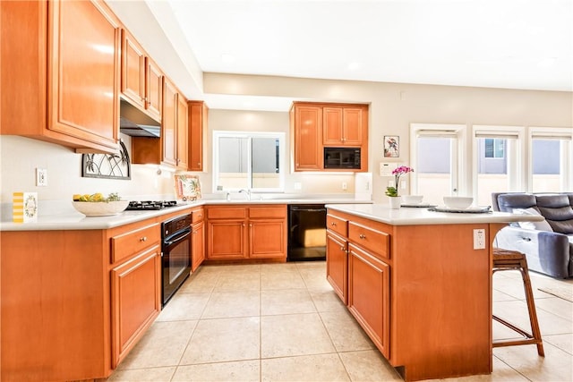 kitchen with light tile patterned floors, a kitchen bar, a center island, black appliances, and sink