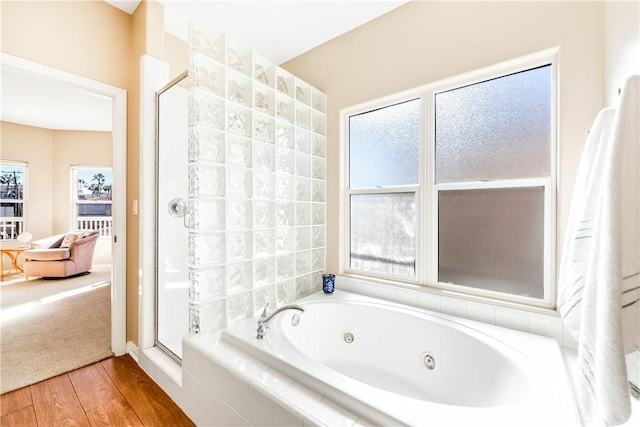 bathroom with a stall shower, a tub with jets, and wood finished floors