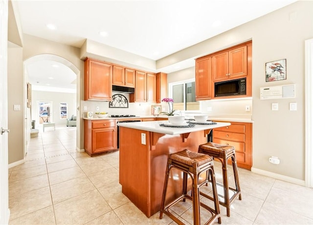 kitchen featuring arched walkways, light tile patterned floors, light countertops, a kitchen island, and black microwave