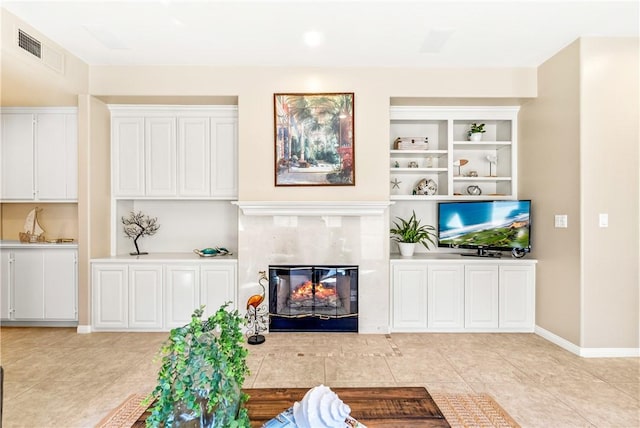 living area with light tile patterned floors, built in shelves, visible vents, baseboards, and a glass covered fireplace