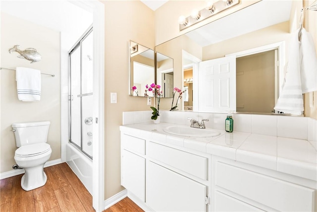 full bath featuring toilet, combined bath / shower with glass door, vanity, wood finished floors, and baseboards