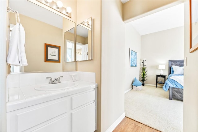 ensuite bathroom with connected bathroom, vanity, baseboards, and wood finished floors