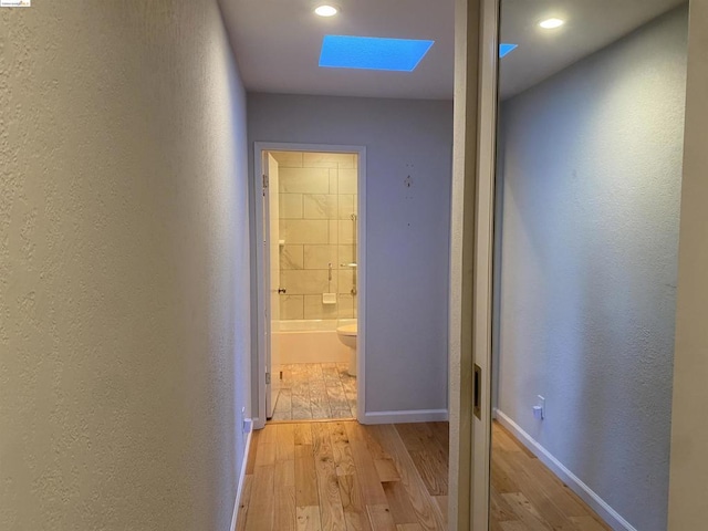 corridor with light hardwood / wood-style floors and a skylight