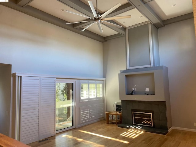 interior space featuring ceiling fan, light hardwood / wood-style floors, a high ceiling, and a tiled fireplace