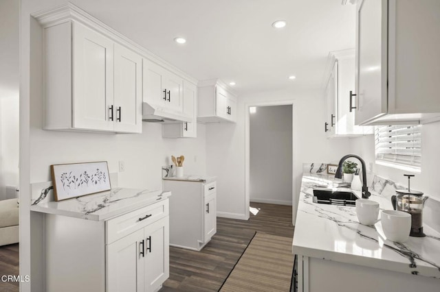 kitchen with light stone countertops, white cabinets, dark wood-type flooring, and sink