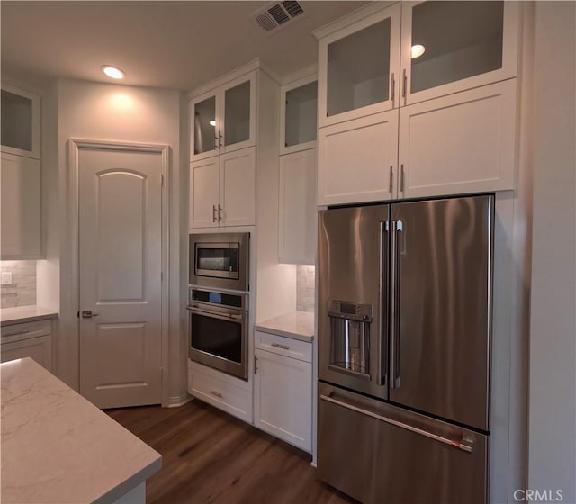 kitchen with decorative backsplash, light stone counters, stainless steel appliances, dark wood-type flooring, and white cabinetry