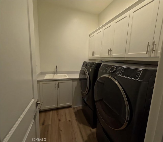 clothes washing area featuring separate washer and dryer, sink, cabinets, and light hardwood / wood-style flooring