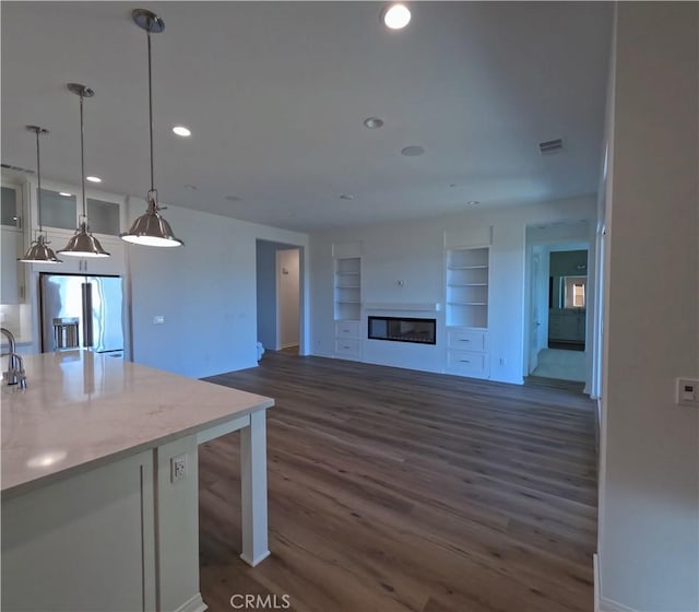 kitchen featuring light stone countertops, stainless steel fridge, pendant lighting, built in features, and dark hardwood / wood-style floors