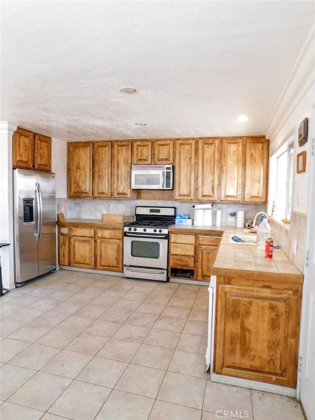 kitchen with tile countertops, sink, decorative backsplash, light tile patterned floors, and stainless steel appliances