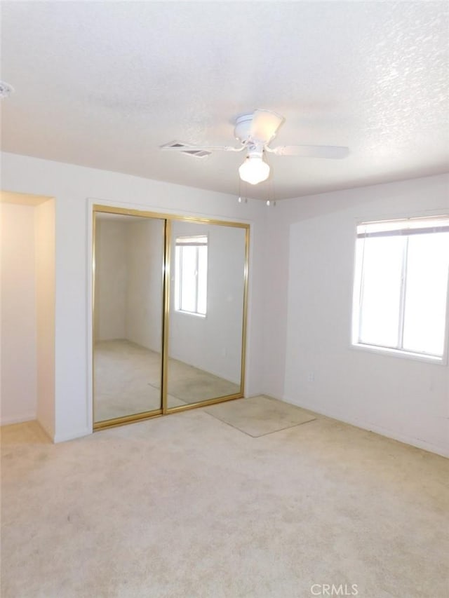 unfurnished bedroom with ceiling fan, a closet, a textured ceiling, and carpet