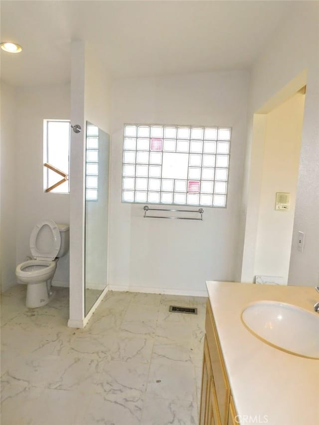 bathroom featuring a healthy amount of sunlight, vanity, toilet, and a shower