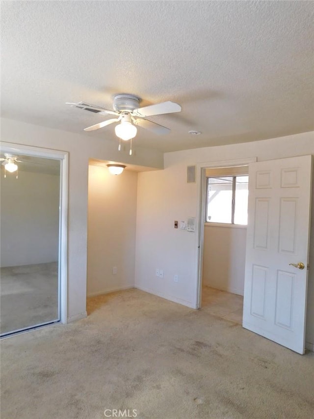 spare room with a textured ceiling, light colored carpet, and ceiling fan