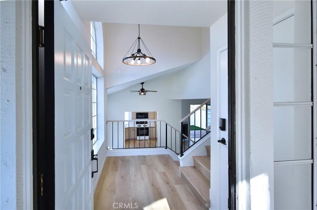 entrance foyer featuring a high ceiling, ceiling fan with notable chandelier, and light hardwood / wood-style flooring