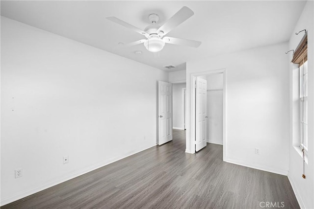 unfurnished bedroom featuring ceiling fan, dark hardwood / wood-style flooring, a walk in closet, and a closet