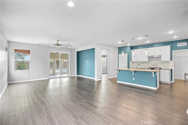 kitchen with ceiling fan, a kitchen breakfast bar, dark hardwood / wood-style floors, an island with sink, and white cabinets