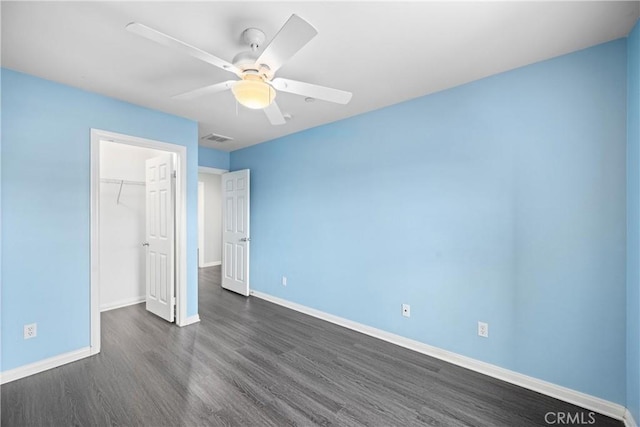 unfurnished bedroom with a walk in closet, a closet, dark hardwood / wood-style floors, and ceiling fan