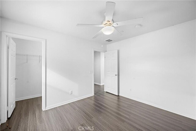 unfurnished bedroom with ceiling fan, a spacious closet, dark wood-type flooring, and a closet