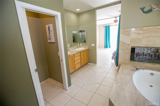 bathroom featuring ceiling fan, tile patterned flooring, tiled bath, a tiled fireplace, and vanity