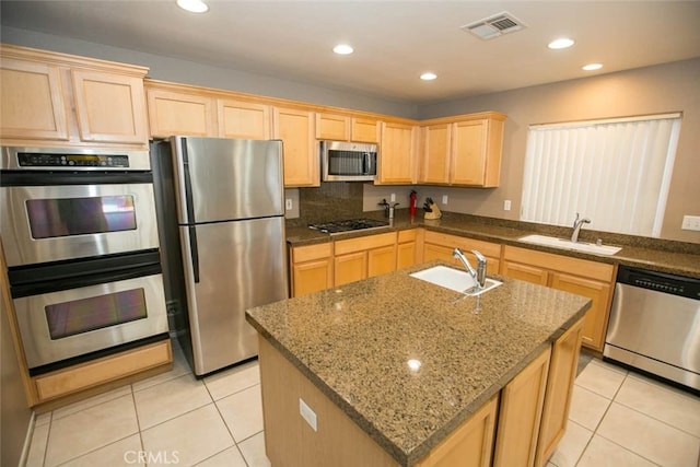 kitchen with stone counters, stainless steel appliances, a kitchen island with sink, and sink