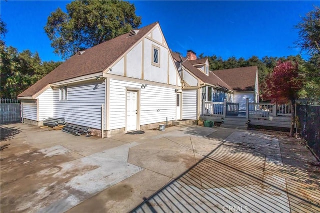 view of home's exterior featuring roof with shingles, a chimney, a patio area, fence, and a deck