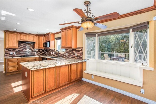 kitchen featuring sink, light stone counters, black appliances, light hardwood / wood-style floors, and kitchen peninsula