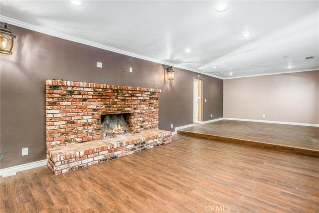 unfurnished living room with hardwood / wood-style flooring, crown molding, and a brick fireplace