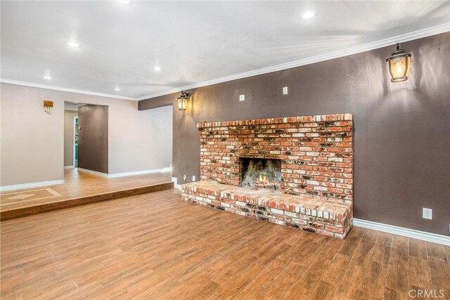 unfurnished living room with wood-type flooring, a brick fireplace, and crown molding