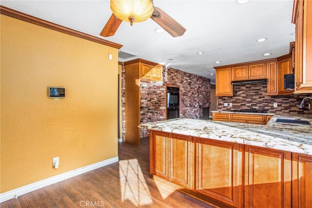 kitchen featuring sink, kitchen peninsula, hardwood / wood-style flooring, light stone countertops, and decorative backsplash