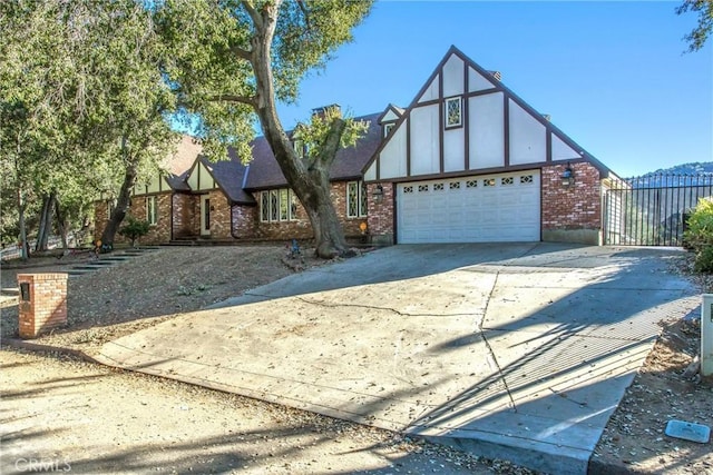 tudor home with a garage, brick siding, fence, driveway, and stucco siding