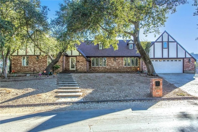 english style home featuring driveway, an attached garage, roof with shingles, and brick siding