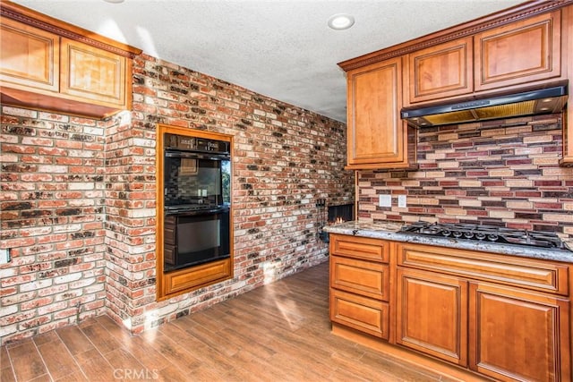 kitchen featuring extractor fan, stone countertops, double oven, and light hardwood / wood-style flooring