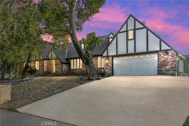 english style home featuring an attached garage, brick siding, a shingled roof, concrete driveway, and stucco siding