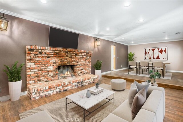 living room featuring hardwood / wood-style flooring, crown molding, and a brick fireplace