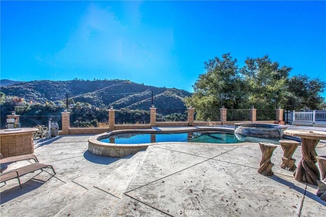 view of pool featuring an in ground hot tub, a mountain view, and a patio