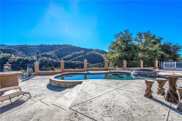 view of swimming pool featuring a pool with connected hot tub, a mountain view, a patio, and fence