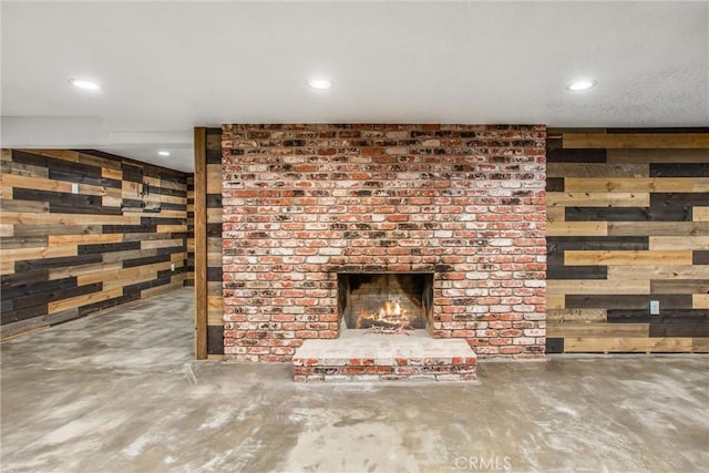 unfurnished living room featuring concrete flooring, recessed lighting, a brick fireplace, and wooden walls