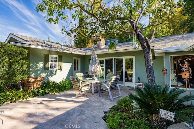 back of house featuring a patio area, outdoor dining area, a chimney, and stucco siding