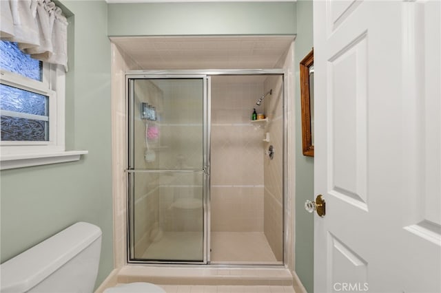 bathroom featuring a shower with door and toilet