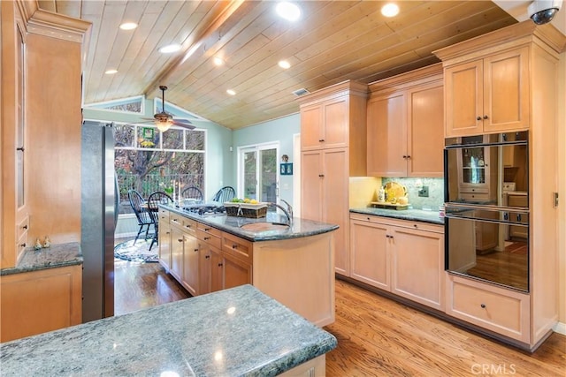 kitchen featuring an island with sink, stainless steel appliances, lofted ceiling with beams, and light wood-style floors