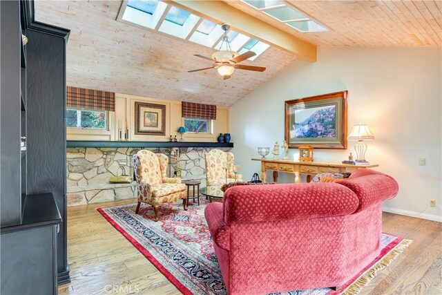 living area featuring lofted ceiling with skylight, baseboards, a ceiling fan, and wood finished floors