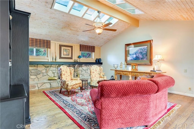 living area featuring lofted ceiling with skylight, wood finished floors, baseboards, and ceiling fan