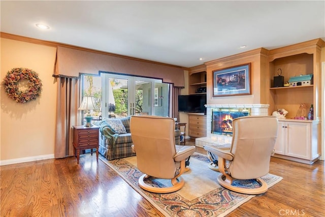 living room featuring french doors, crown molding, a glass covered fireplace, and light wood finished floors