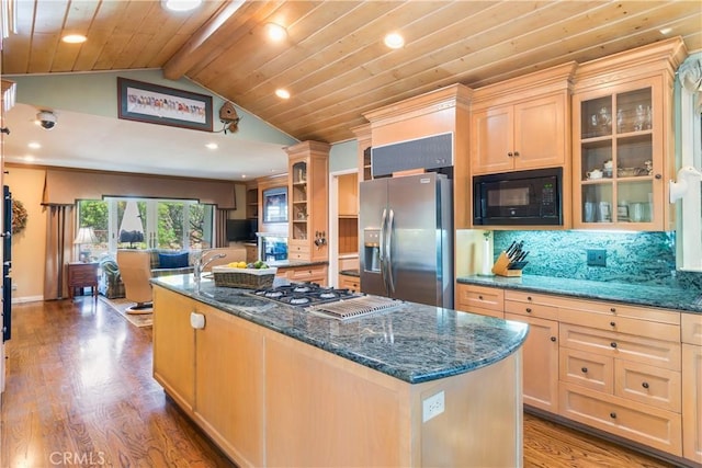 kitchen with wood finished floors, lofted ceiling with beams, a kitchen island with sink, stainless steel appliances, and tasteful backsplash