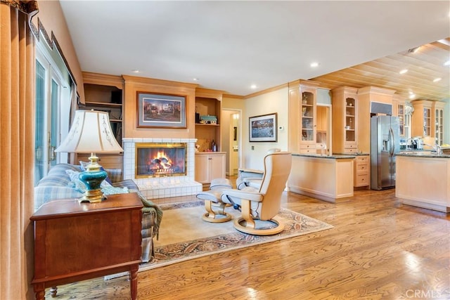 living area with a tiled fireplace, recessed lighting, light wood finished floors, and ornamental molding