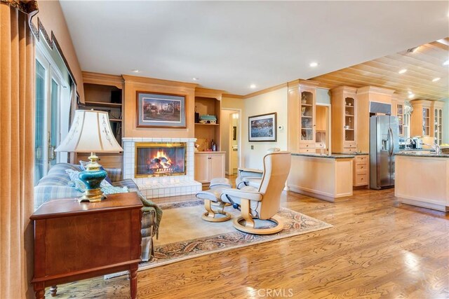 living room featuring recessed lighting, light wood finished floors, ornamental molding, a fireplace, and built in features