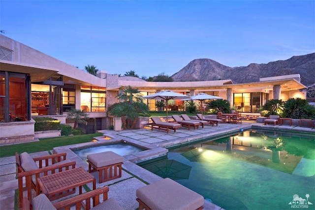 pool at dusk with a mountain view, a patio, and an in ground hot tub