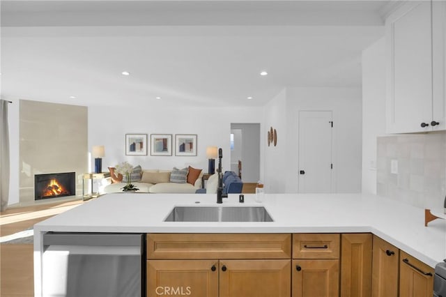 kitchen featuring sink, tasteful backsplash, white cabinetry, stainless steel dishwasher, and a tiled fireplace