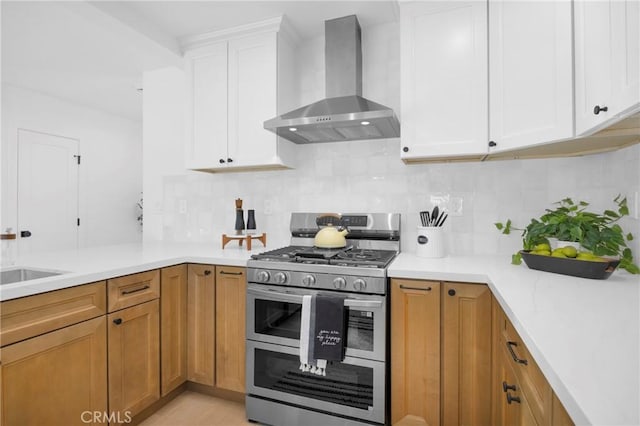 kitchen with wall chimney range hood, sink, white cabinetry, tasteful backsplash, and range with two ovens